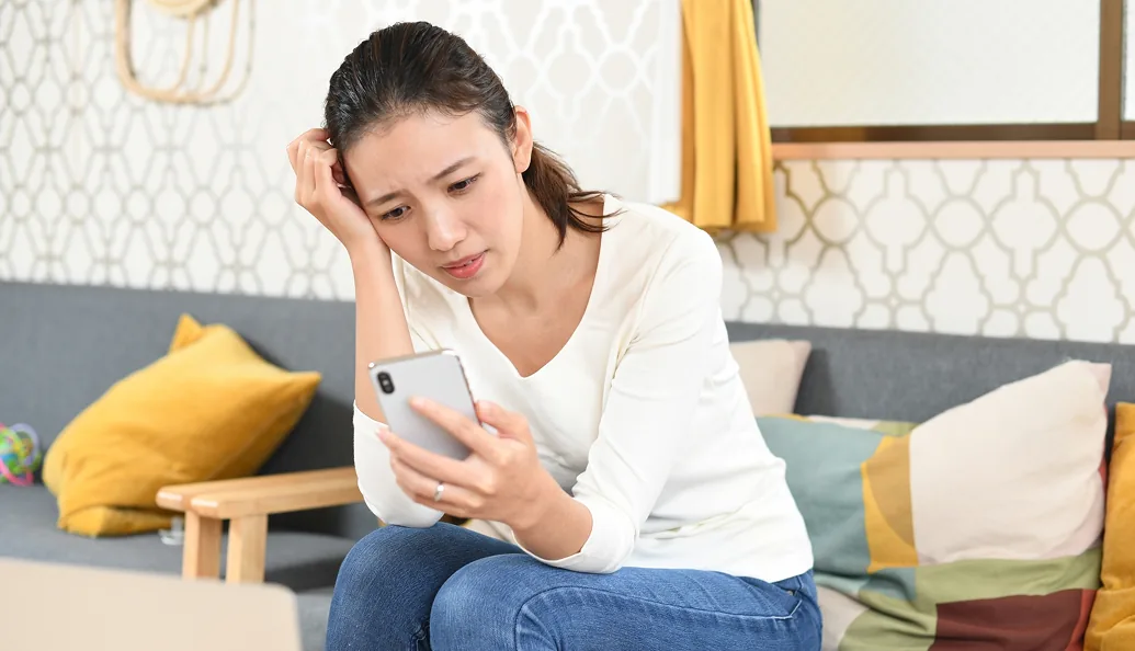 スマートフォンを見ながら悩む女性